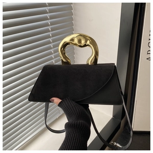 Detail view of sculptural gold metal handle on a black suede minimalist handbag