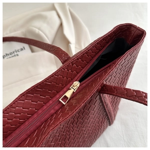 Detail of wine red woven tote bag showing golden zipper closure and texture