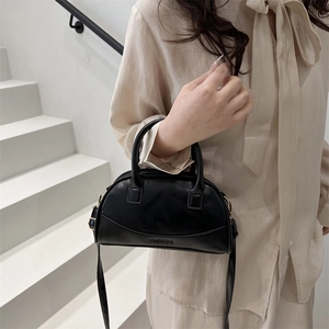 Minimalist black leather Boston handbag with FASHION embossing held by a model