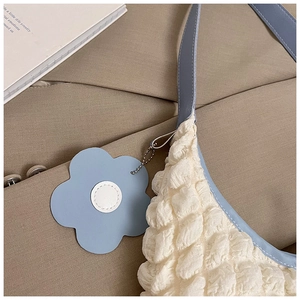 Detail of white popcorn textured tote bag with light blue trim and floral charm decoration