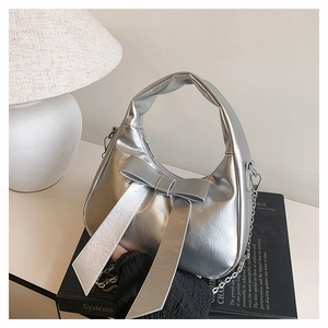 Detail of silver metallic handbag featuring a large bow and detachable chain strap