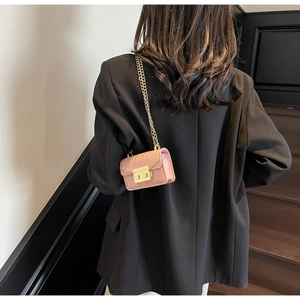 Mini sac bandoulière rose avec chaîne dorée et fermoir porté sur un blazer noir