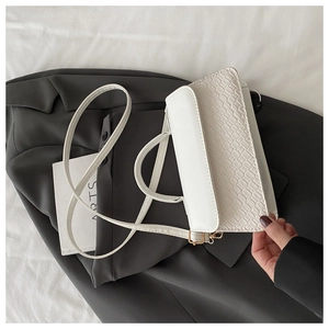 Detail of white faux leather crossbody bag with crocodile pattern flap on grey suit
