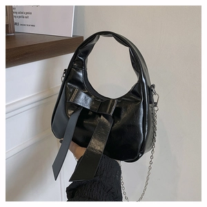 Detail of black glossy patent leather hobo bag with oversized bow and metal chain strap