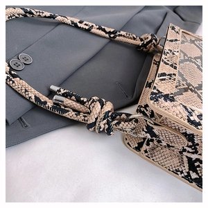 Macro shot of faux leather crossbody bag with snake print texture and knotted strap detail