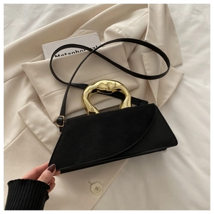Detail of minimalist black matte handbag featuring sculptural gold wavy metal handle