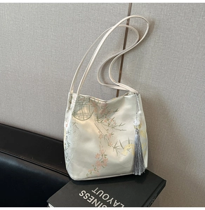 Detail of satin bucket bag featuring floral embroidery and grey tassel with beads