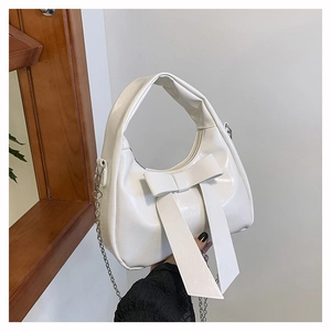 Close-up of a white glossy leather hobo bag with a large bow and silver chain strap