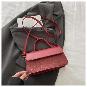 Detail of dark red crossbody bag with snake texture over a grey blazer and art book
