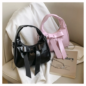 Detail of glossy dumpling bag featuring oversized bow and metallic chain strap