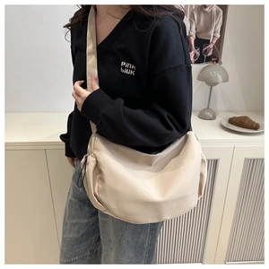 Détail d'un sac demi-lune en nylon beige porté en bandoulière, soulignant texture et taille