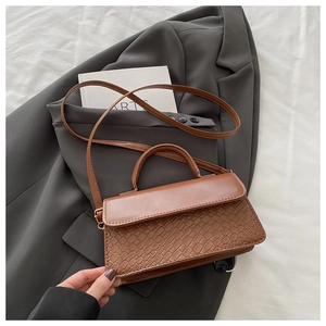 Close-up of brown leather bag showing woven texture and gold hardware on white cloth