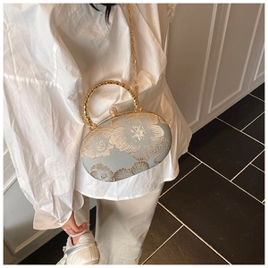 Detail of grey shell clutch bag with gold flower embroidery and metallic circular handle