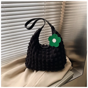 Close-up of black bubble textured tote bag with a green flower charm on fabric