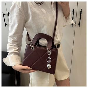 Detail of burgundy quilted leather handbag with silver metallic charms and round handles