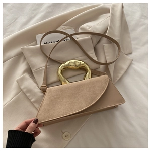 Detail of a trapezoid leather bag with sculptural gold metal handle on beige blazer
