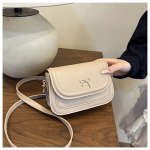 Detail of a beige crossbody bag with a golden bow clasp held against a desk