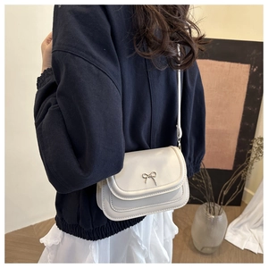 Detailed view of a cream white crossbody bag with a silver metallic bow on the flap