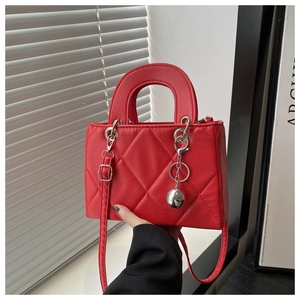 Close-up of red quilted handbag featuring silver ball charm and textured faux leather