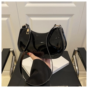 Detail of glossy black patent leather crescent shoulder bag with golden metal zipper