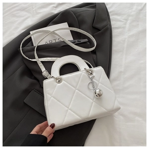 Detail of white quilted handbag with silver sphere charm and elegant top handle