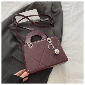 Detailed view of burgundy quilted faux leather bag with round handle and silver charm