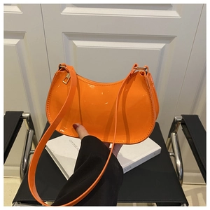 Detail of bright orange patent leather shoulder bag with sleek glossy finish and gold hardware