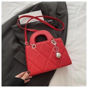 Detail of red quilted PU leather crossbody bag with silver ball charm on grey blazer