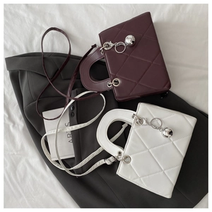 Detail of quilted leather handbag featuring metal sphere charm and top handle
