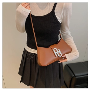 Detail of a brown leather shoulder bag featuring a prominent silver metal monogram clasp