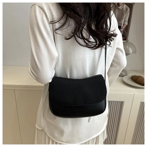 Model wearing a minimalist black matte leather crossbody bag with a curved flap design
