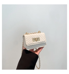 Detail of white chevron quilted handbag featuring gold metal turn-lock and chain strap