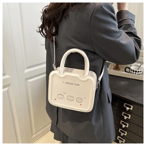 Détail d'un sac bandoulière blanc imprimé ours porté sur une veste de costume grise