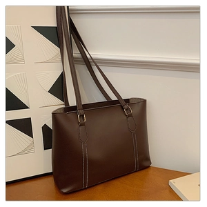 Détail d'un sac cabas marron foncé mat avec surpiqûres blanches et boucles dorées