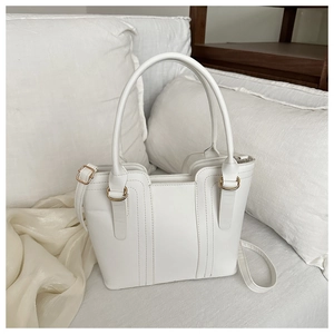 Détail d'un cabas en cuir blanc avec anneaux dorés posé sur des draps blancs doux