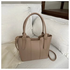 Détail du sac seau matelassé beige avec ferrures dorées sur un canapé blanc