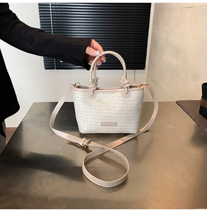 Dettaglio di una borsa a secchiello in paglia intrecciata beige con manico in pelle