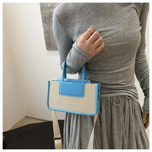 Detail of canvas crossbody bag showing contrast leather handles and woven strap
