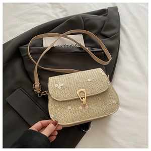 Dettaglio della borsa in paglia beige con ricami floreali rosa e chiusura in metallo dorato