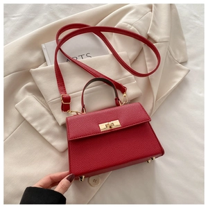 Detail of red litchi texture handbag featuring gold clasp and structured top handle