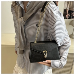 Detail of black crocodile texture crossbody bag with gold metal buckle and chain strap