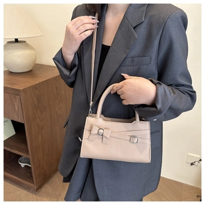 Detail showing the beige crossbody bag with bow design worn by a model in a casual suit