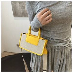 Detail of canvas crossbody bag with contrast yellow trim worn by a model in gray