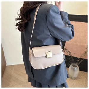 Détail d'un sac à bandoulière beige avec boucle dorée sur un mannequin en blazer