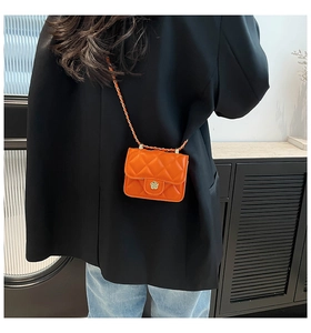 Detail of quilted orange mini crossbody bag with a floral metal clasp and chain strap