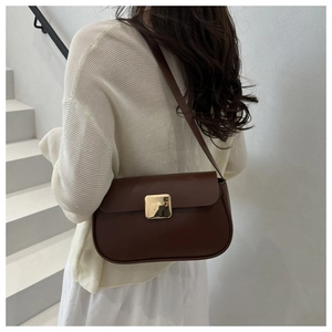 Detail of a dark brown leather shoulder bag with a gold square buckle on a model