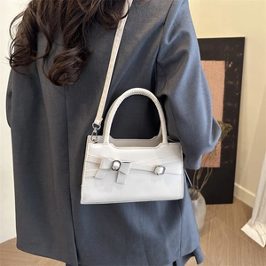Sac à main blanc en cuir avec boucle nœud porté par un mannequin, style épuré