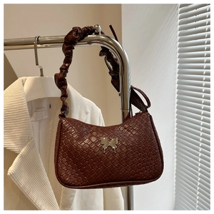 Detail of dark brown woven texture with silver butterfly ornament on pleated handbag