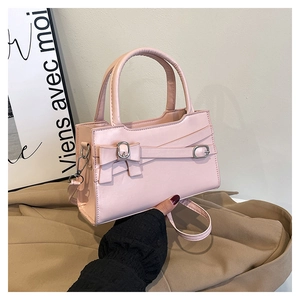 Detail of light pink crossbody bag with bow accent and metallic buckle on art board