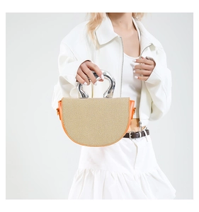 Détail du sac à main en paille tressée avec bordure en cuir orange et poignée argentée
